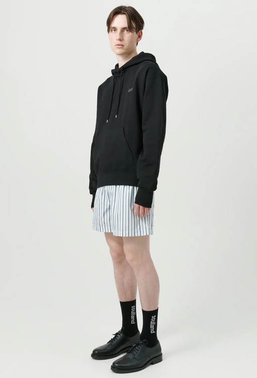 A man wearing a soulland hoodie with short striped shorts and black shoes