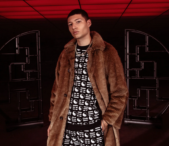 A man wearing a clot fur coat and branded yin and yang all over print shirt