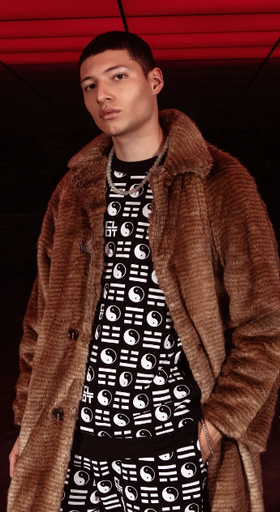 A man wearing a clot fur coat and branded yin and yang all over print shirt