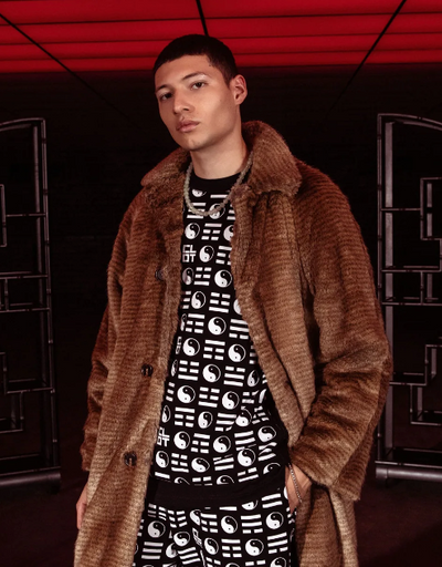 A man wearing a clot fur coat and branded yin and yang all over print shirt