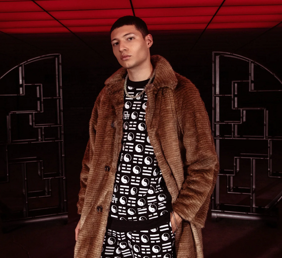 A man wearing a clot fur coat and branded yin and yang all over print shirt