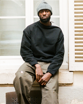 A man wearing a Spencer Badu black sweater and dark green pants