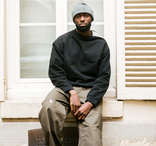 A man wearing a Spencer Badu black sweater and dark green pants