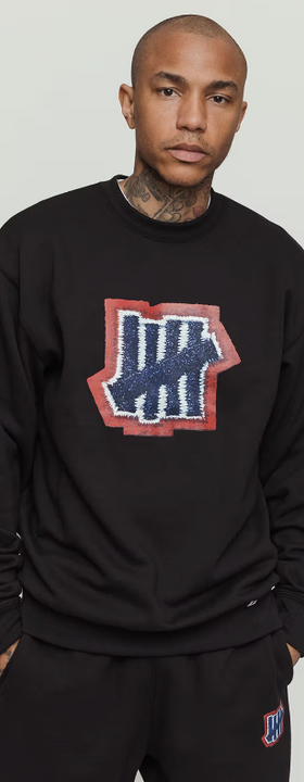 A man wearing an undefeated logo black sweater
