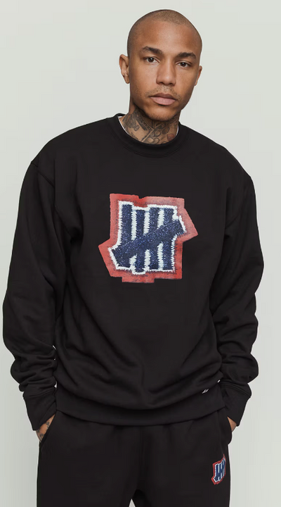 A man wearing an undefeated logo black sweater