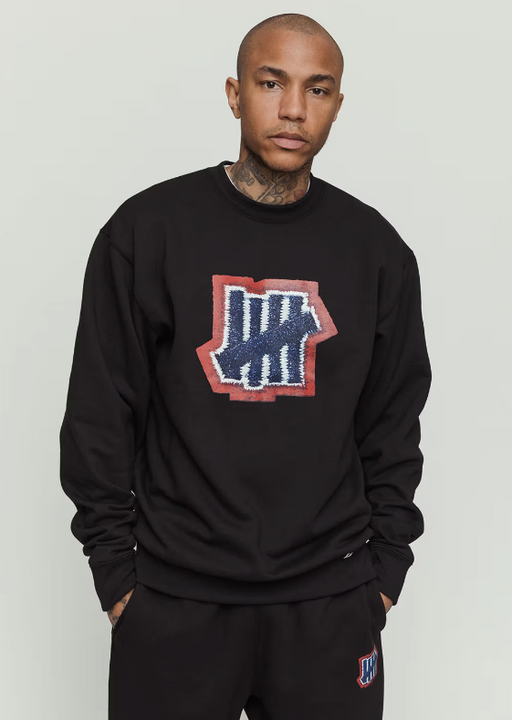 A man wearing an undefeated logo black sweater