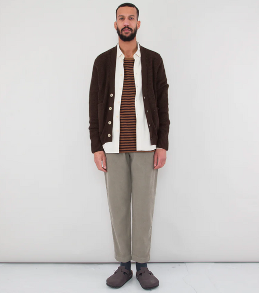 A man wearing a Folk Clothing layered outfit with a brown cardigan and white button up and grey pants