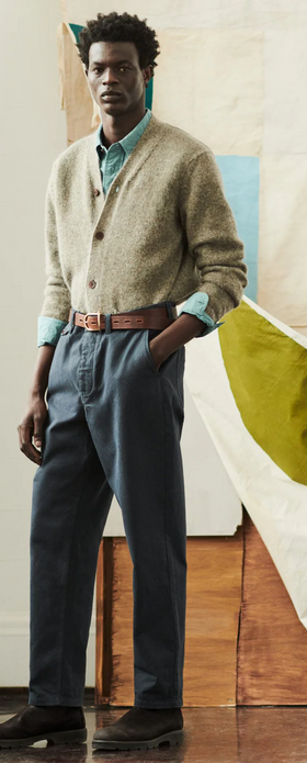 A man wearing a Toast clothing outfit featuring a beige cardigan and dark blue pants with a brown belt