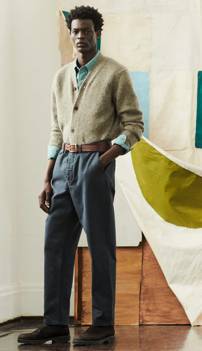 A man wearing a Toast clothing outfit featuring a beige cardigan and dark blue pants with a brown belt