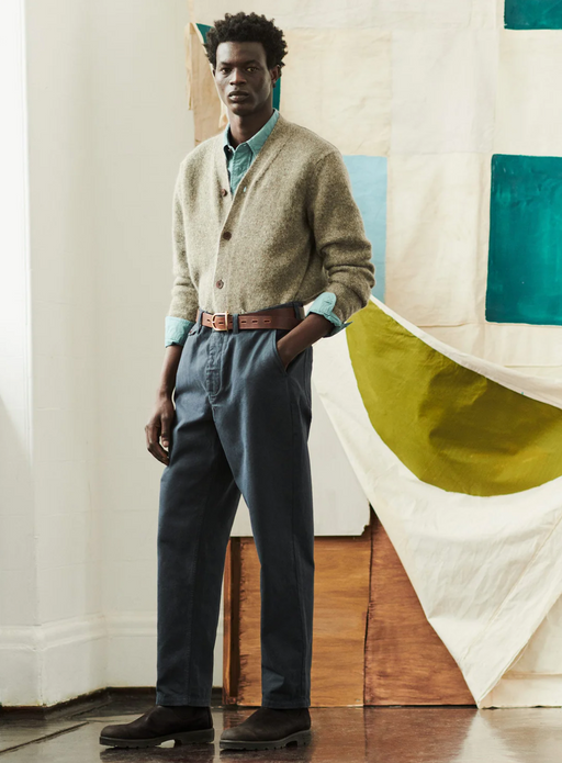 A man wearing a Toast clothing outfit featuring a beige cardigan and dark blue pants with a brown belt