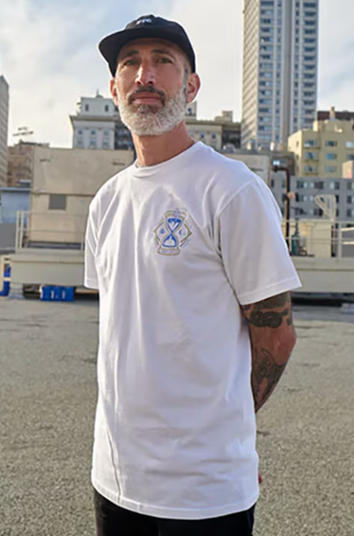 A man standing wearing a Benny Gold white t-shirt and black hat