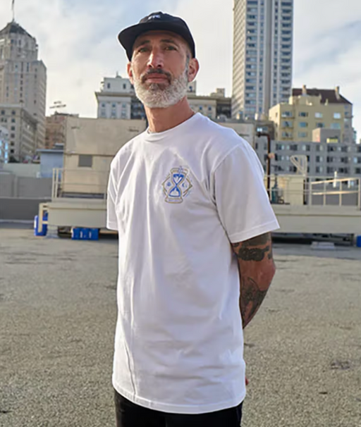 A man standing wearing a Benny Gold white t-shirt and black hat