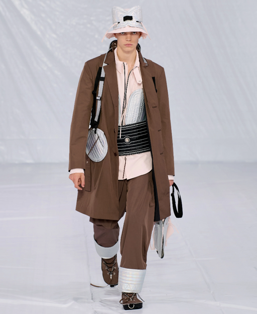 A man walking a runway in a Craig Green designer construction-influenced brown outfit with an overcoat and wide pants