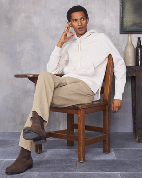 A man sitting in a chair wearing a minamilist Officine Generale white hoodie and khaki pants along with brown boots