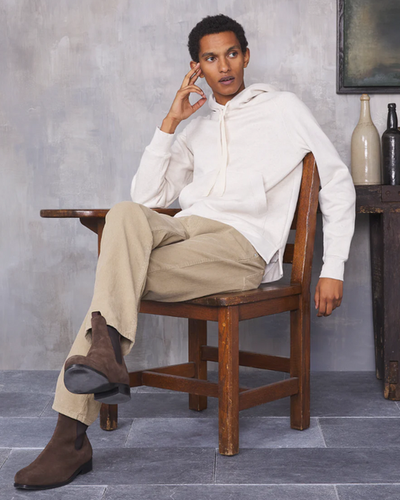 A man sitting in a chair wearing a minamilist Officine Generale white hoodie and khaki pants along with brown boots