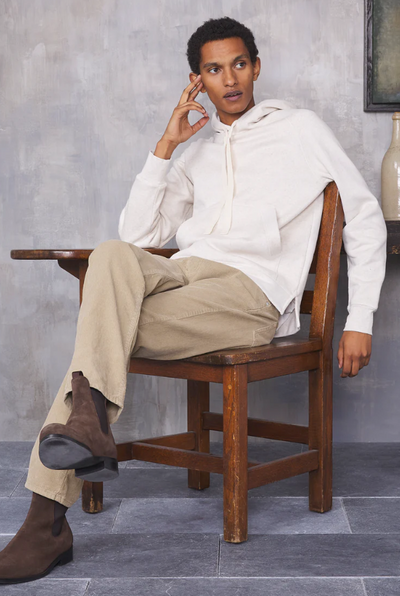 A man sitting in a chair wearing a minamilist Officine Generale white hoodie and khaki pants along with brown boots