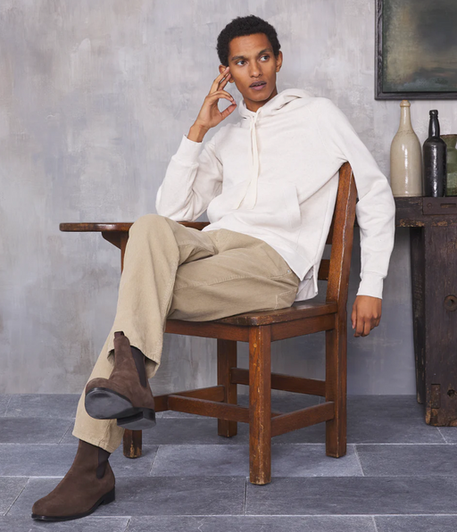 A man sitting in a chair wearing a minamilist Officine Generale white hoodie and khaki pants along with brown boots