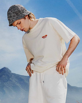 A man wearing a cream Permanent Vacation t-shirt with white pants