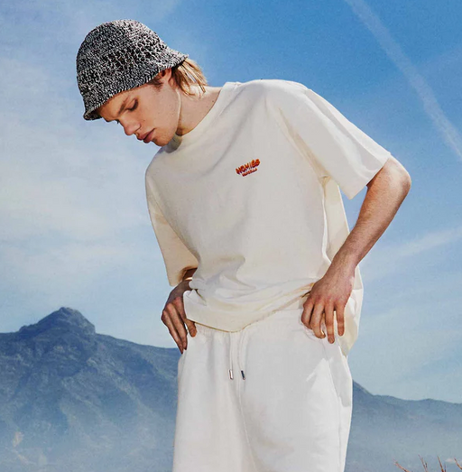 A man wearing a cream Permanent Vacation t-shirt with white pants