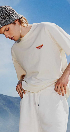 A man wearing a cream Permanent Vacation t-shirt with white pants
