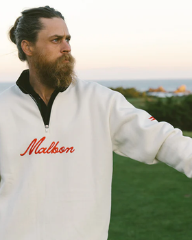 A man wearing a white Malbon golf sweater and golf glove