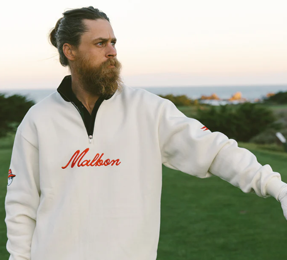 A man wearing a white Malbon golf sweater and golf glove