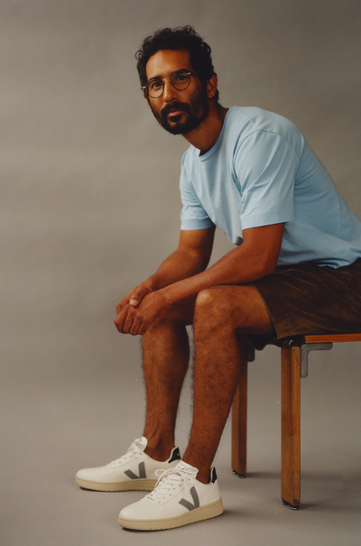 A man wearing a light blue Veja t-shirt with shorts and Veja logo white shoes