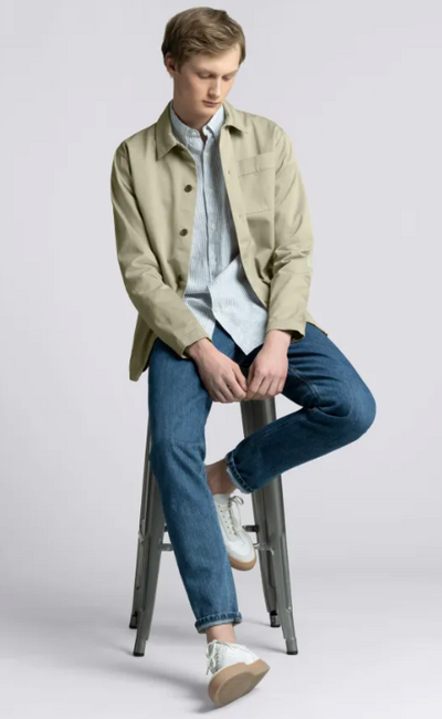 A man wearing an Asket green jacket and blue pants