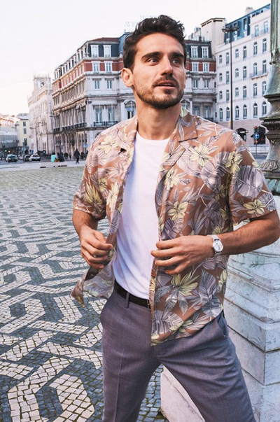 A man wearing a floral Bonobos button-up with a white t-shirt and grey slacks