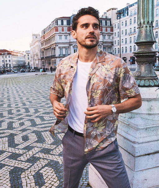 A man wearing a floral Bonobos button-up with a white t-shirt and grey slacks