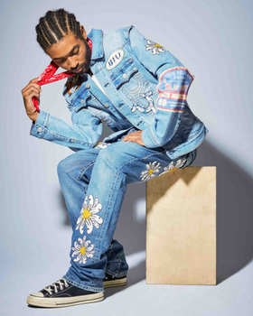 A man wearing a True Religion jean jacket and matching pants with flowers embroidered on it