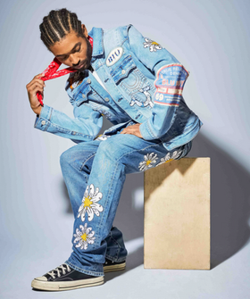 A man wearing a True Religion jean jacket and matching pants with flowers embroidered on it