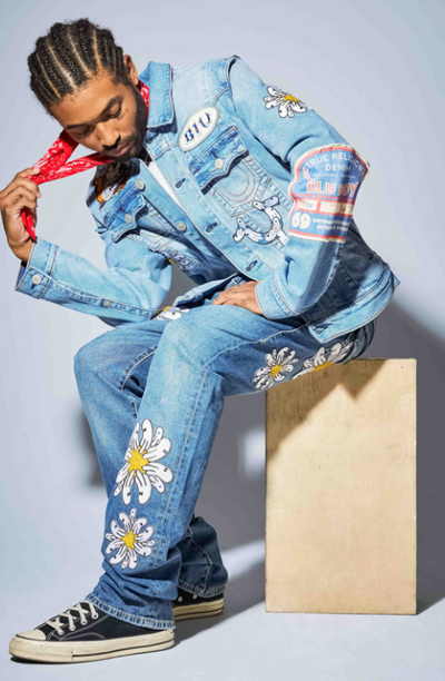A man wearing a True Religion jean jacket and matching pants with flowers embroidered on it