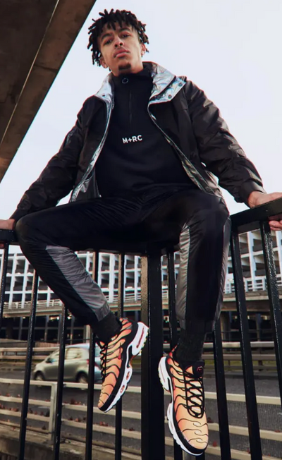 A man wearing a m+rc noir baclk fleece, jacket and track pants