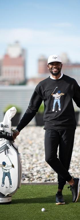 A man golfing wearing a Eastside Golf outfit featuring a sweater and hat