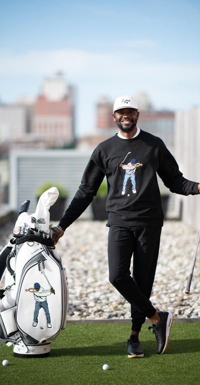 A man golfing wearing a Eastside Golf outfit featuring a sweater and hat