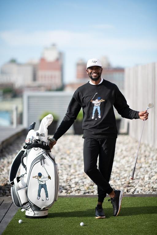A man golfing wearing a Eastside Golf outfit featuring a sweater and hat
