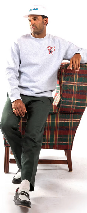 A man wearing a grey Metalwood Studio sweater, a white hat and green slacks