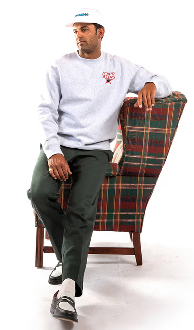 A man wearing a grey Metalwood Studio sweater, a white hat and green slacks