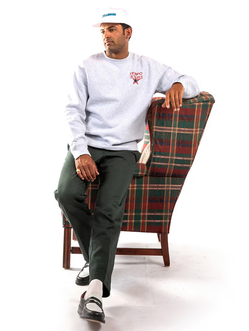 A man wearing a grey Metalwood Studio sweater, a white hat and green slacks