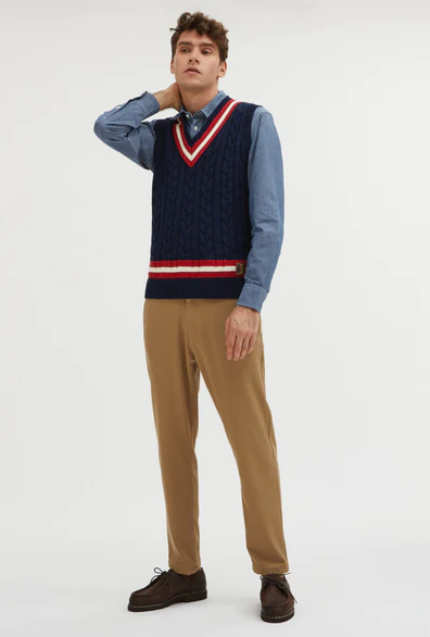 A man wearing a preppy vest from Baracuta and brown slacks