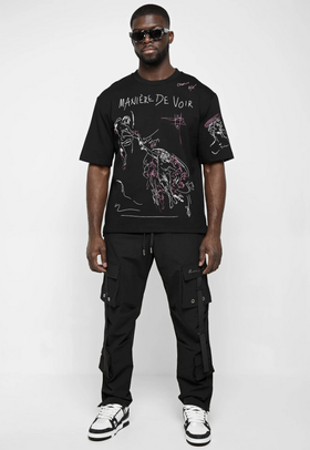 A man wearing a black Maniere De Voir illustrated t-shirt