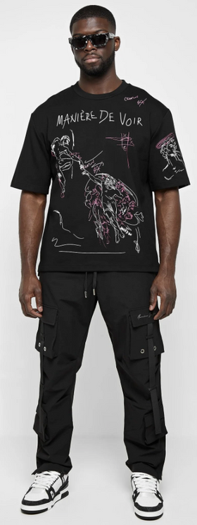 A man wearing a black Maniere De Voir illustrated t-shirt