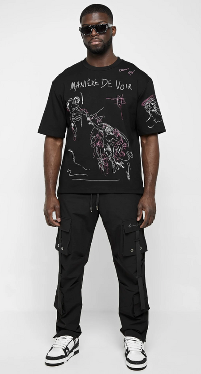 A man wearing a black Maniere De Voir illustrated t-shirt