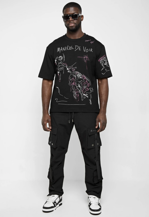 A man wearing a black Maniere De Voir illustrated t-shirt
