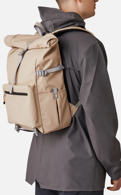 A man wearing a Sandqvist beige backpack and dark grey rain coat