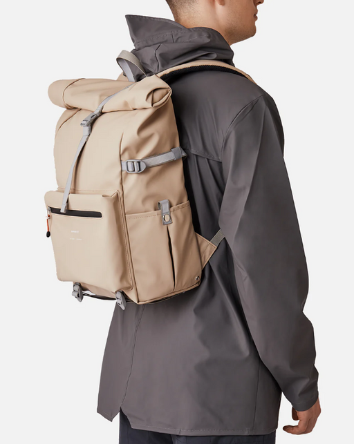 A man wearing a Sandqvist beige backpack and dark grey rain coat