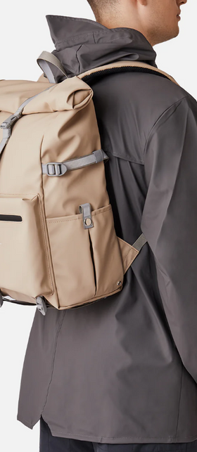 A man wearing a Sandqvist beige backpack and dark grey rain coat