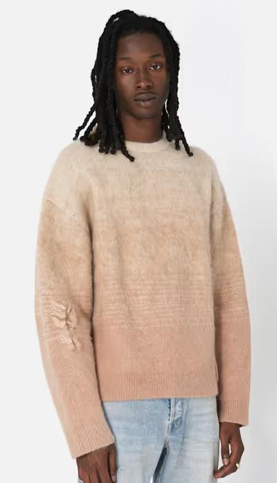 A man wearing a beige gradient sweater and light blue jeans