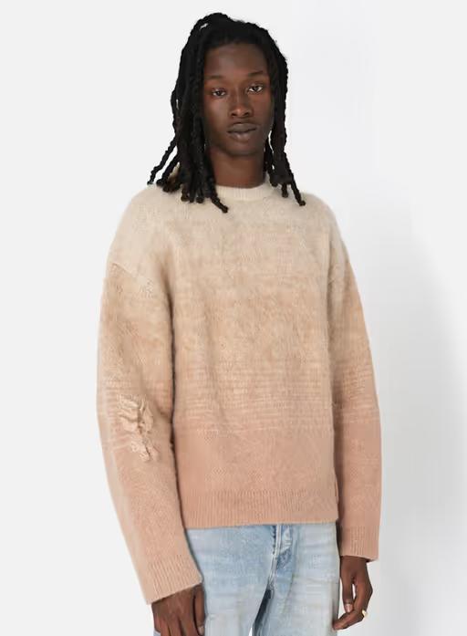 A man wearing a beige gradient sweater and light blue jeans